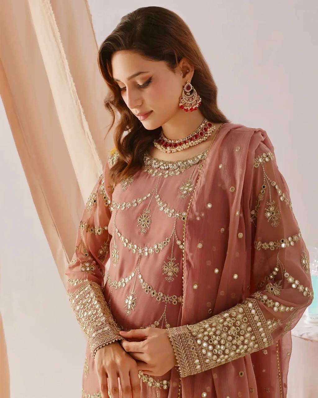 Woman wearing a pink embroidered traditional outfit with gold details.