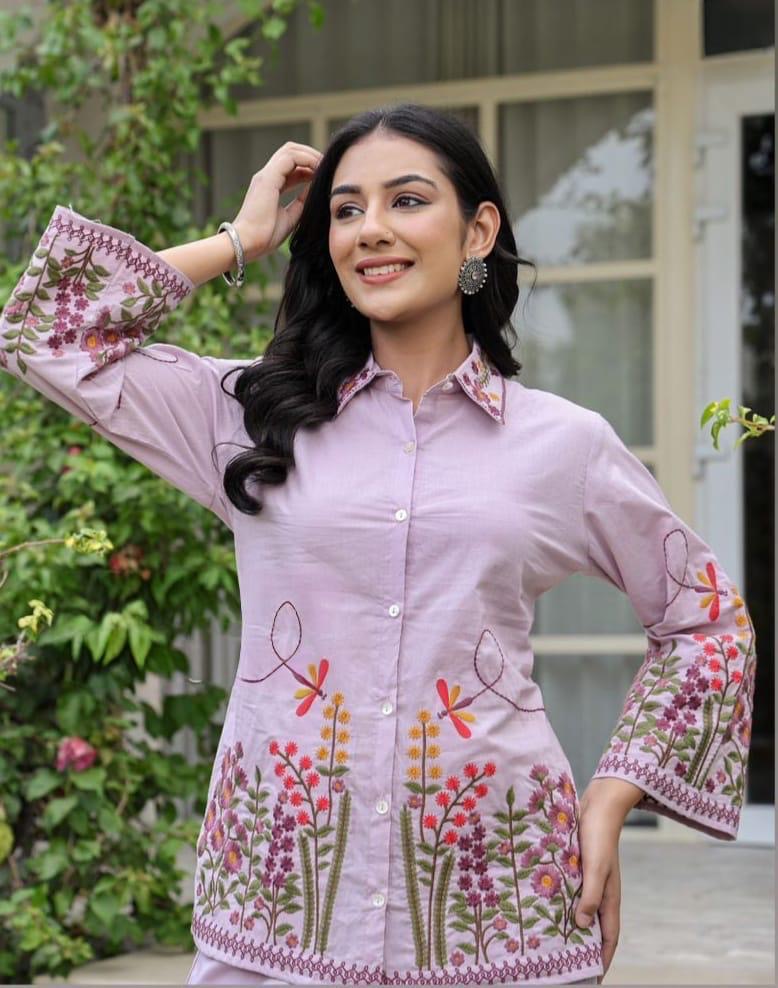 Woman wearing a pink embroidered shirt with floral patterns outdoors.