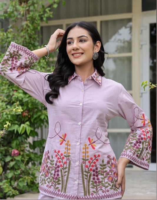 Woman wearing a pink embroidered shirt with floral patterns outdoors.
