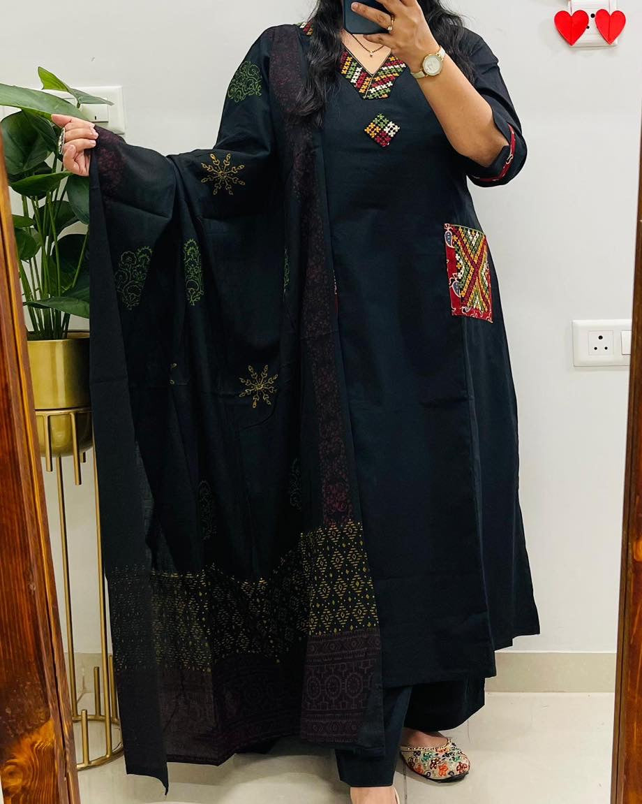 Person wearing a black embroidered outfit holding a matching dupatta in a room.