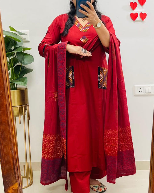 Person wearing a red traditional outfit with intricate patterns, standing in a room.