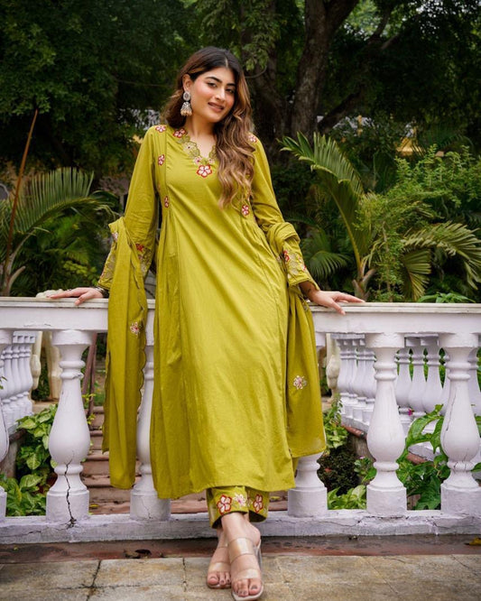 Woman in a green traditional outfit standing on a stone pathway with greenery in the background