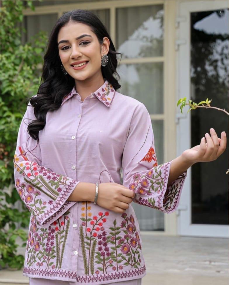 Woman wearing a light purple embroidered shirt with floral patterns outdoors.