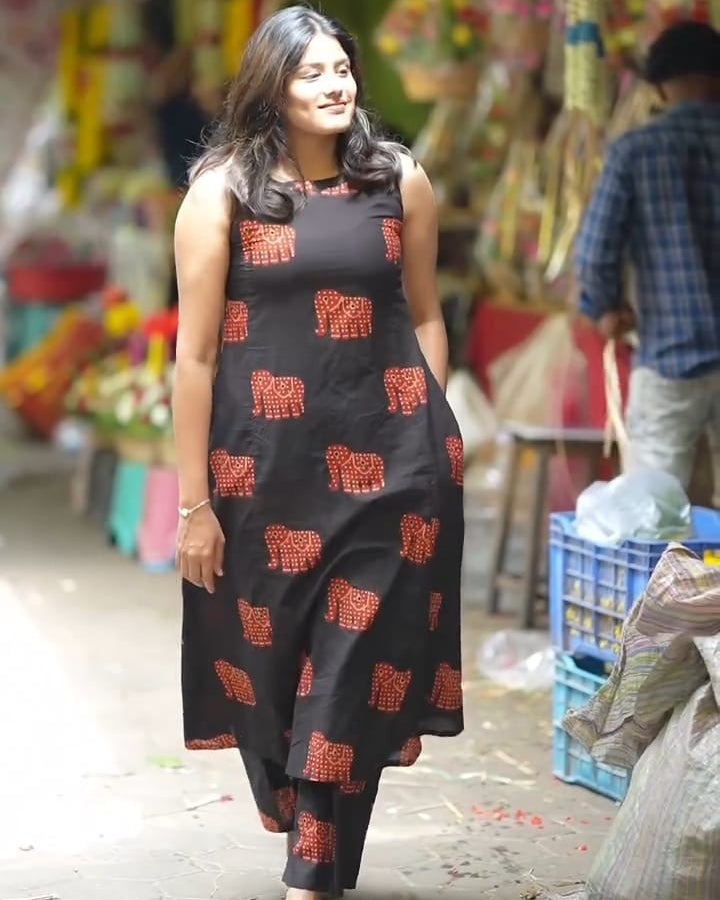 Woman in a black dress with red patterns walking through a market.