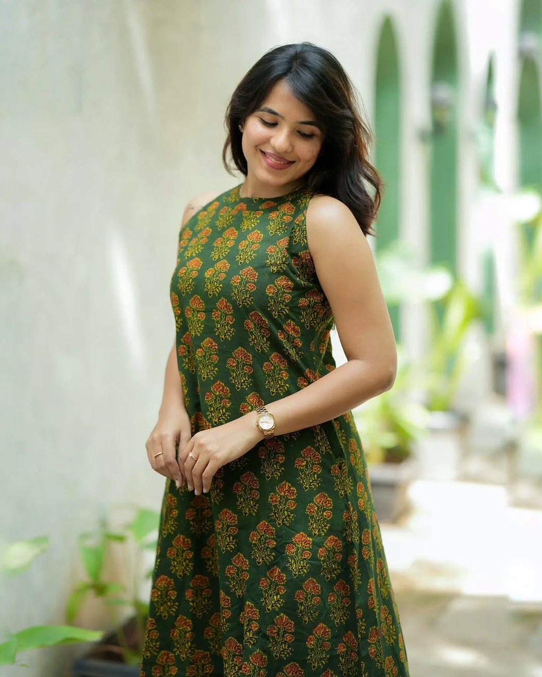 Woman wearing a green patterned dress standing outdoors with plants in the background