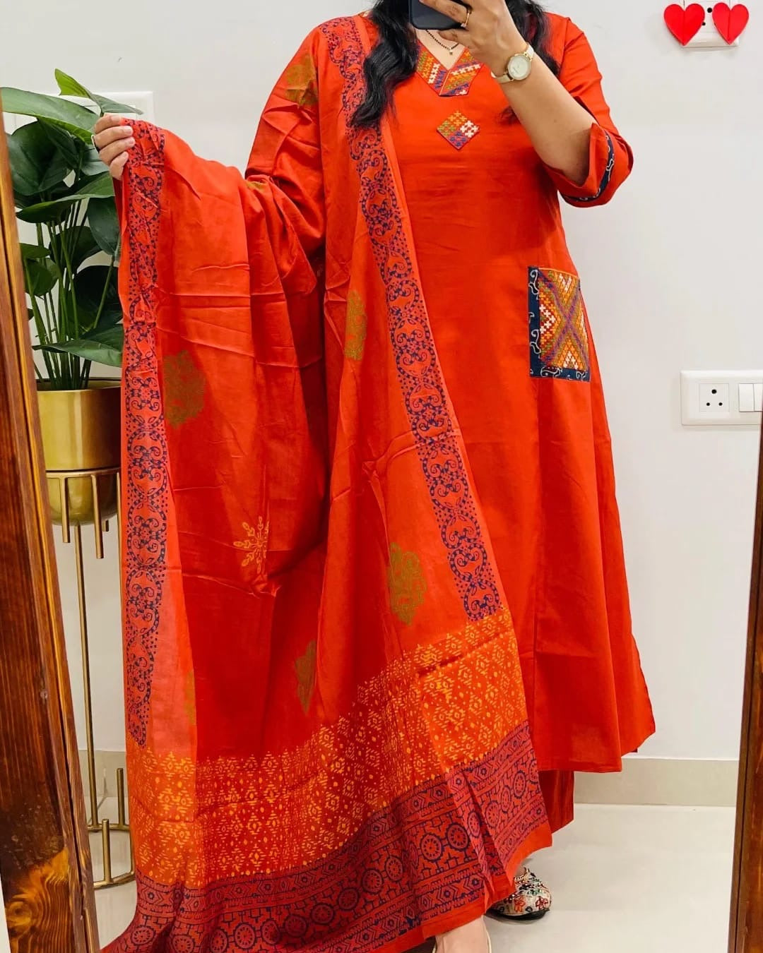 Person wearing an orange traditional outfit with a matching dupatta indoors.