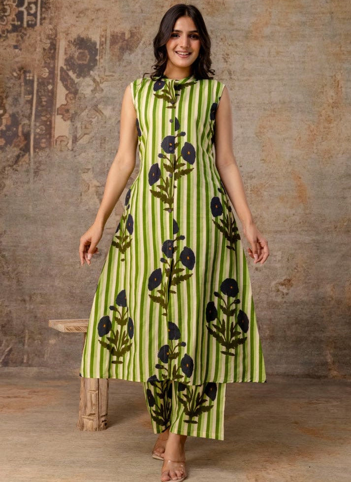 Woman wearing a green dress with black floral patterns against a textured wall.