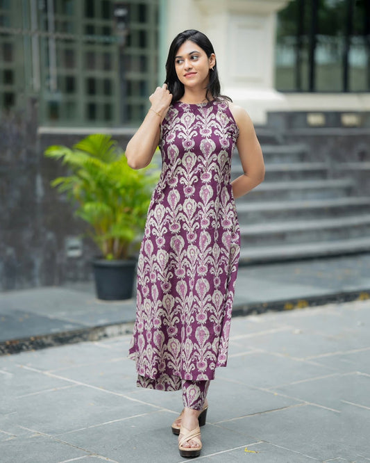 Woman wearing a purple patterned dress standing outdoors on a stone path.