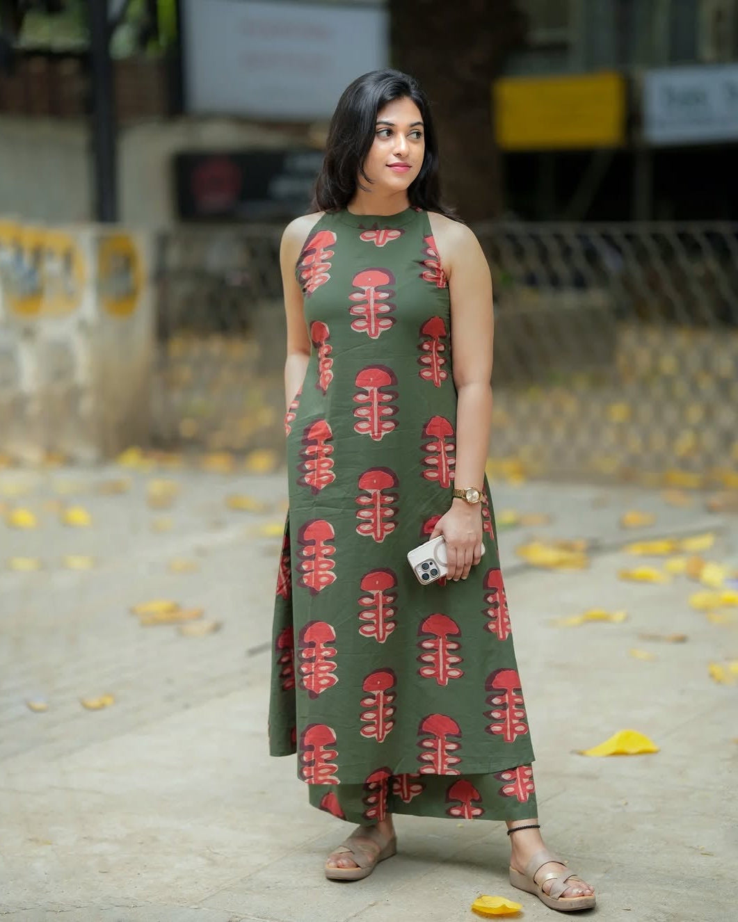 Woman wearing a green dress with red patterns on a street.