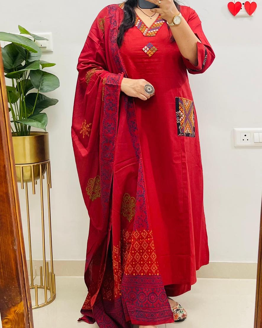 Person wearing a red embroidered saree with a white wall and plant in the background