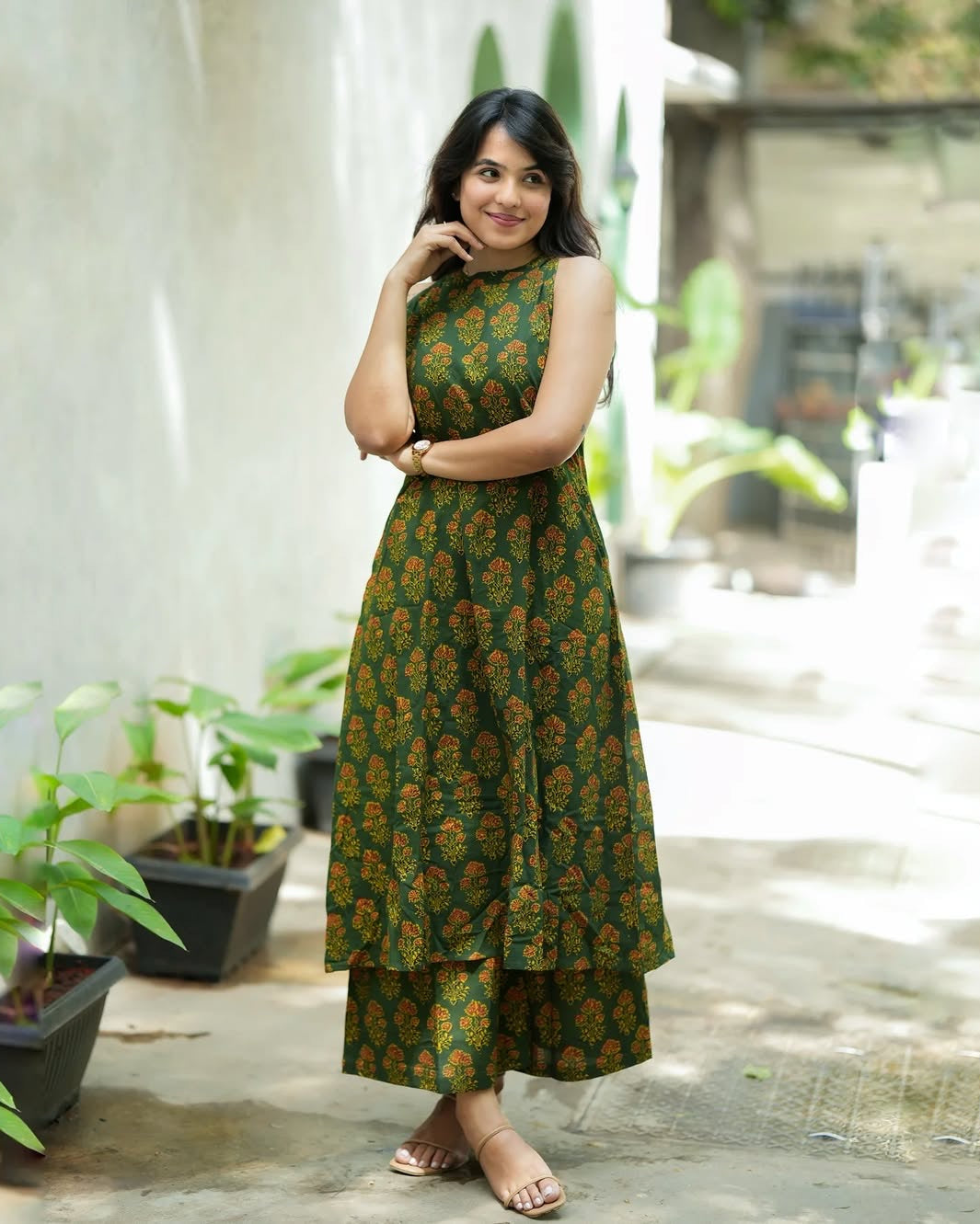 Woman wearing a green floral dress standing outdoors with plants in the background