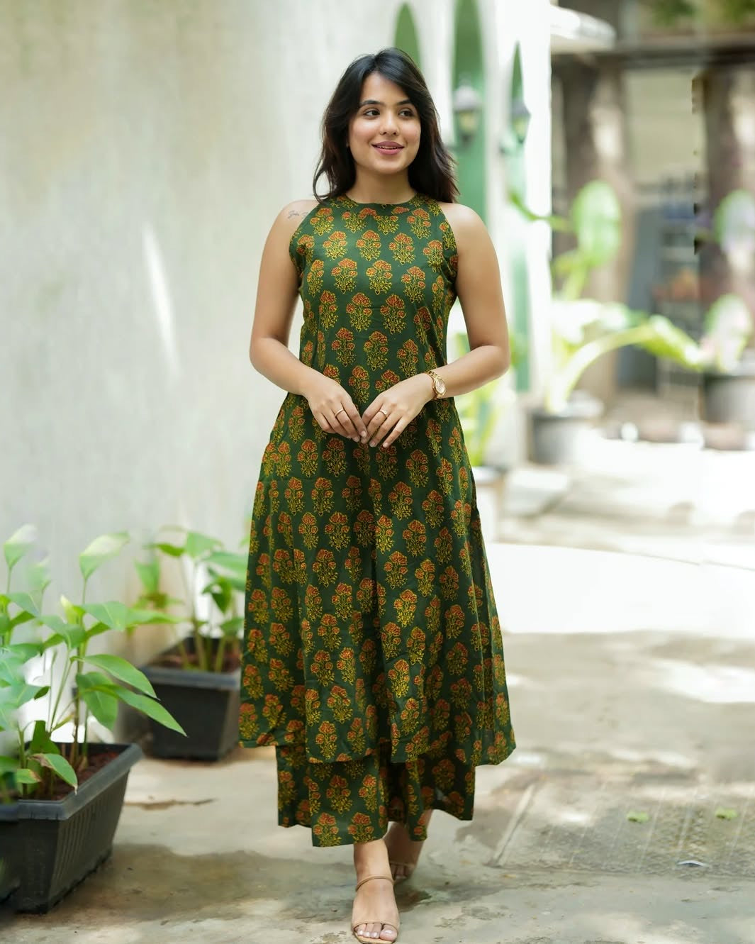 Woman wearing a green floral dress standing outdoors with plants in the background