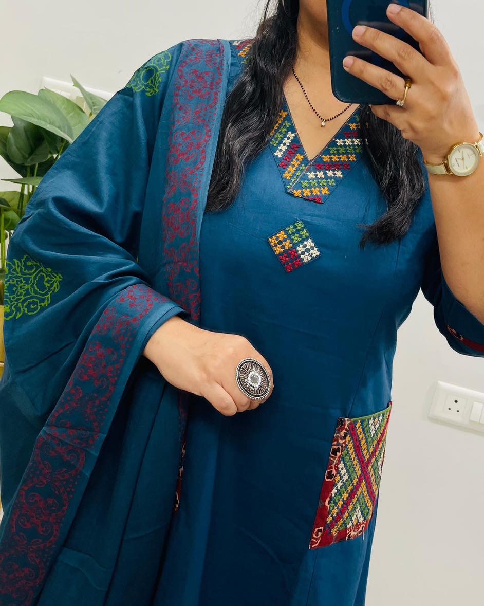 Person wearing a blue embroidered traditional outfit with colorful patterns.