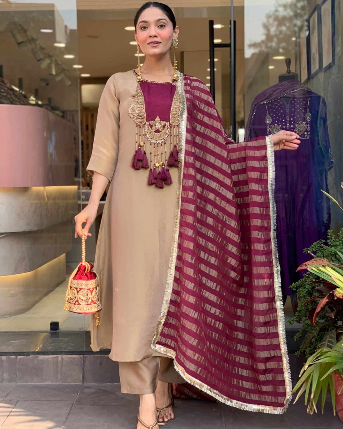 Woman in traditional outfit with a maroon dupatta, standing indoors.