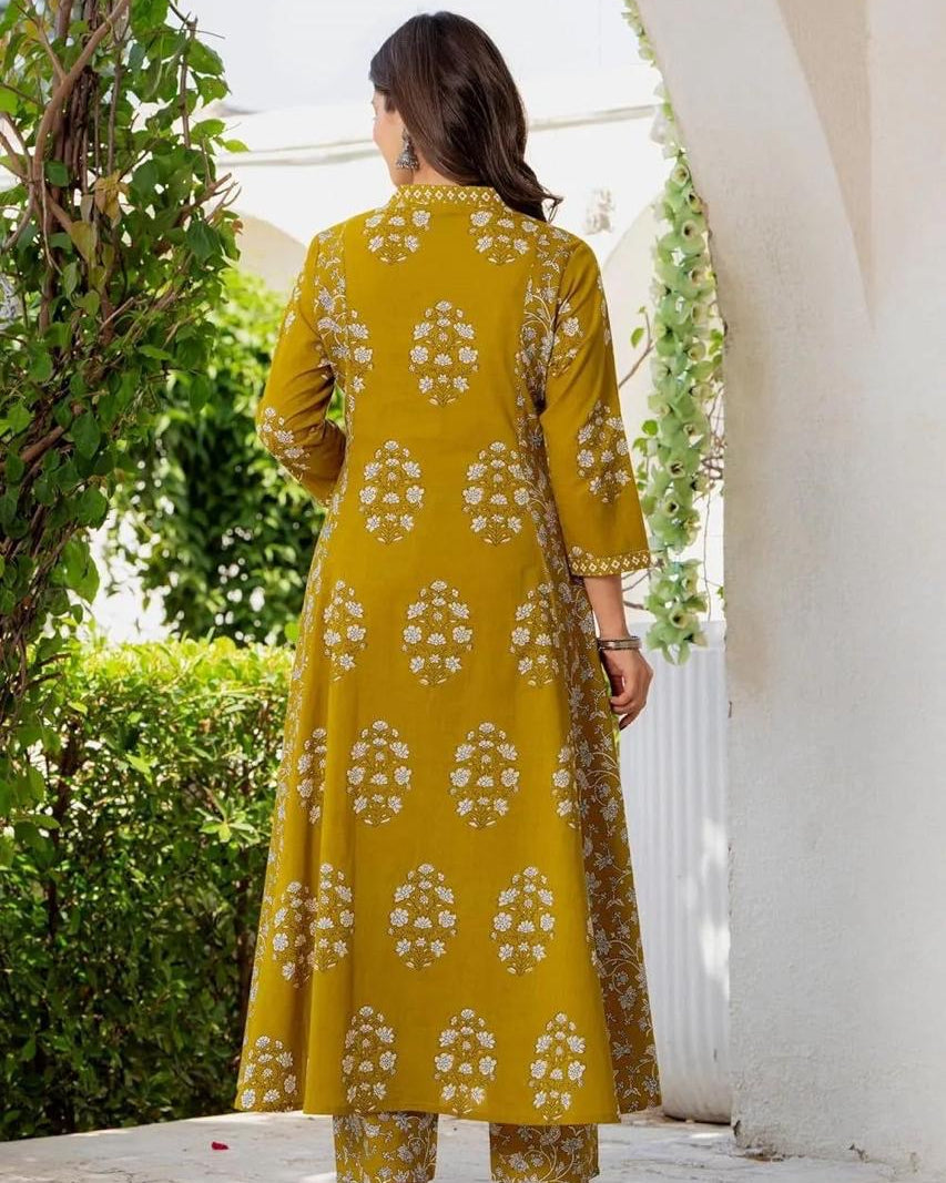 Woman wearing a yellow floral patterned outfit standing outdoors near a white archway.