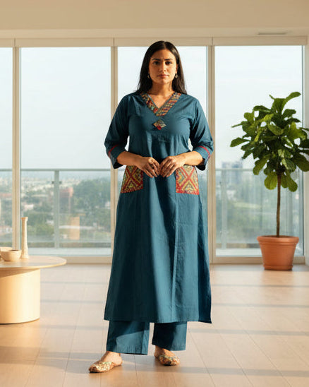 Woman wearing a blue kurta with embroidered pockets indoors.