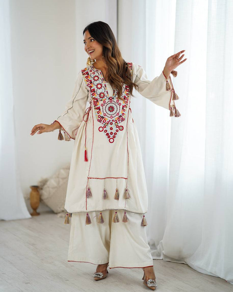 Woman wearing a traditional embroidered outfit with tassels in a bright room.