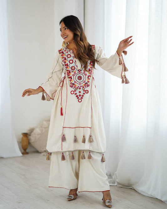 Woman wearing a traditional embroidered outfit with tassels in a bright room.