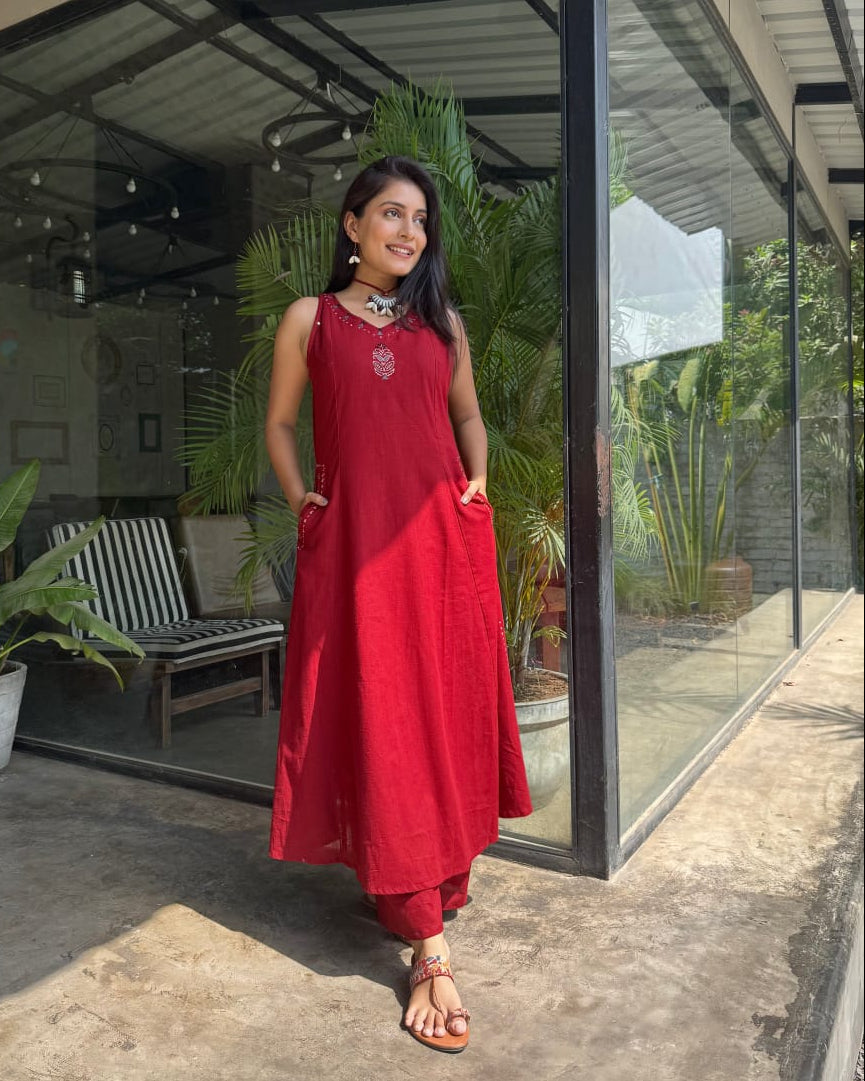 Woman in a red dress standing in front of a glass door with plants around.