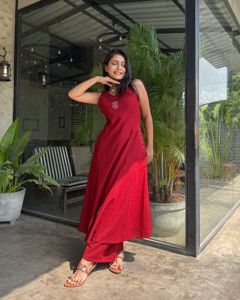 Woman in a red outfit standing in front of a glass door with plants around.