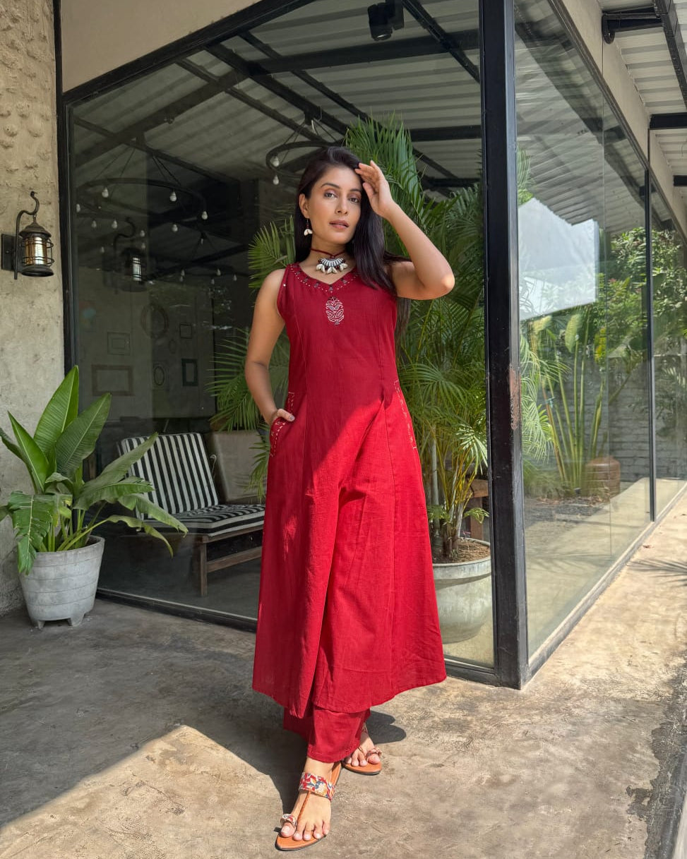 Woman in a red dress standing in front of a glass door with plants around.