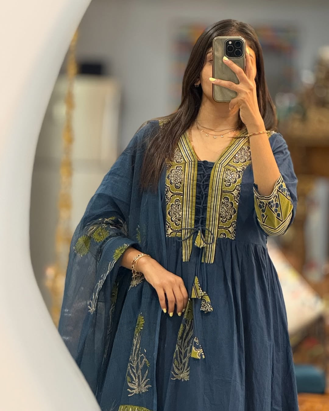 Woman taking a mirror selfie wearing a blue embroidered dress.