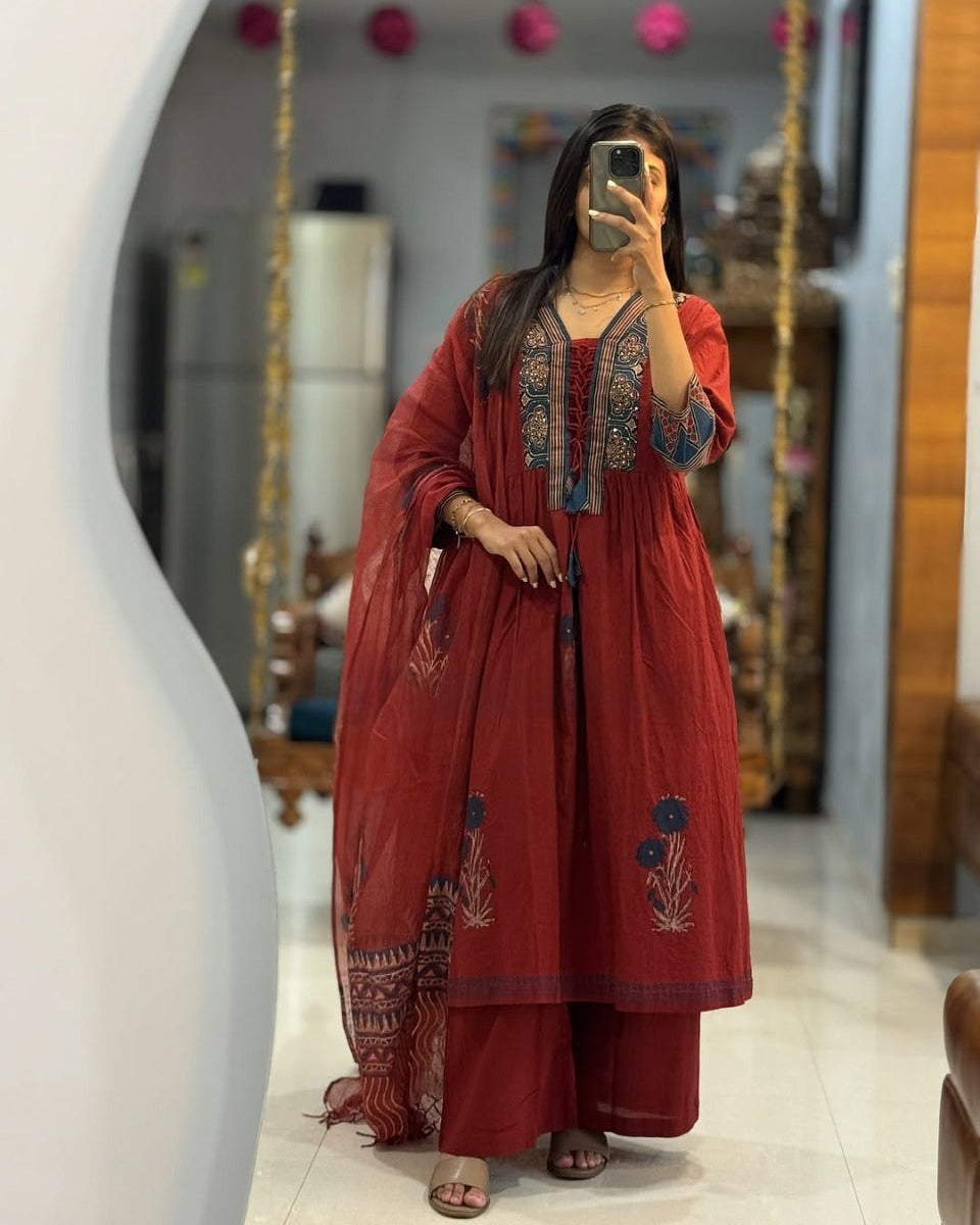 Woman taking a mirror selfie wearing a red embroidered outfit in a home setting.