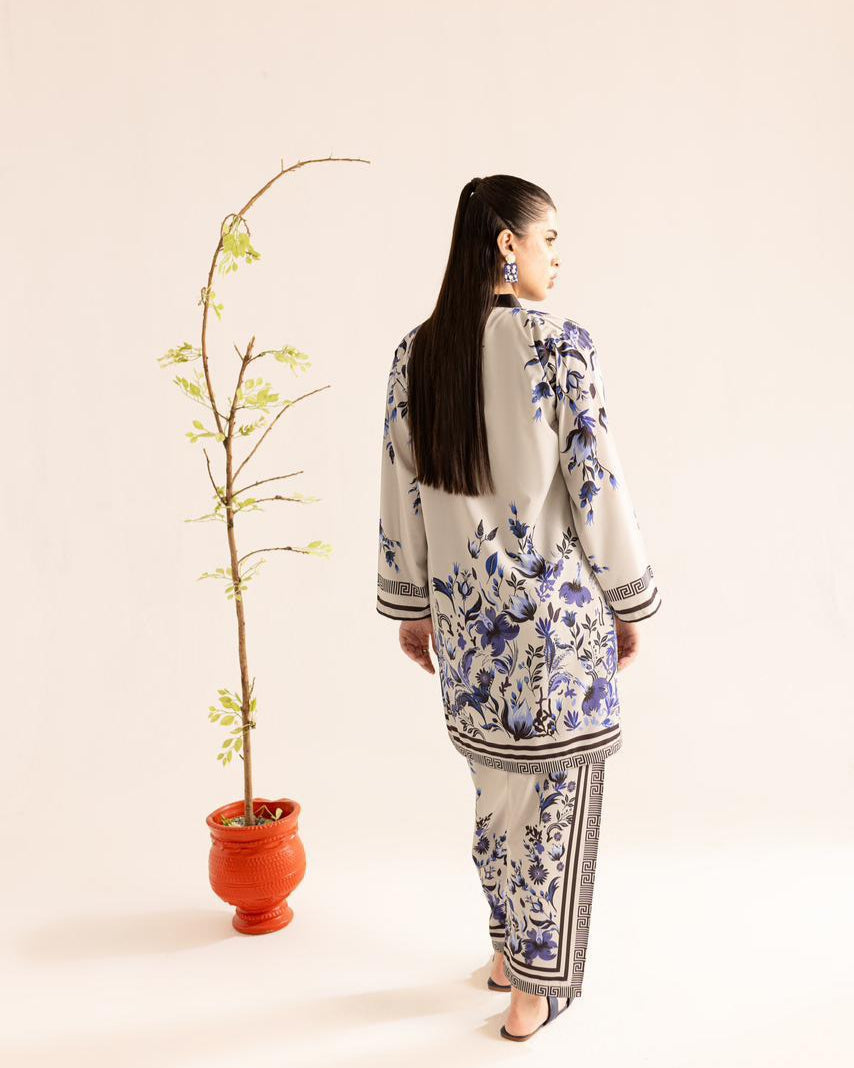 Woman wearing a floral outfit standing next to a potted plant on a plain background