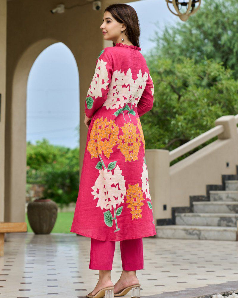 Woman wearing a pink floral outfit standing outdoors with greenery in the background