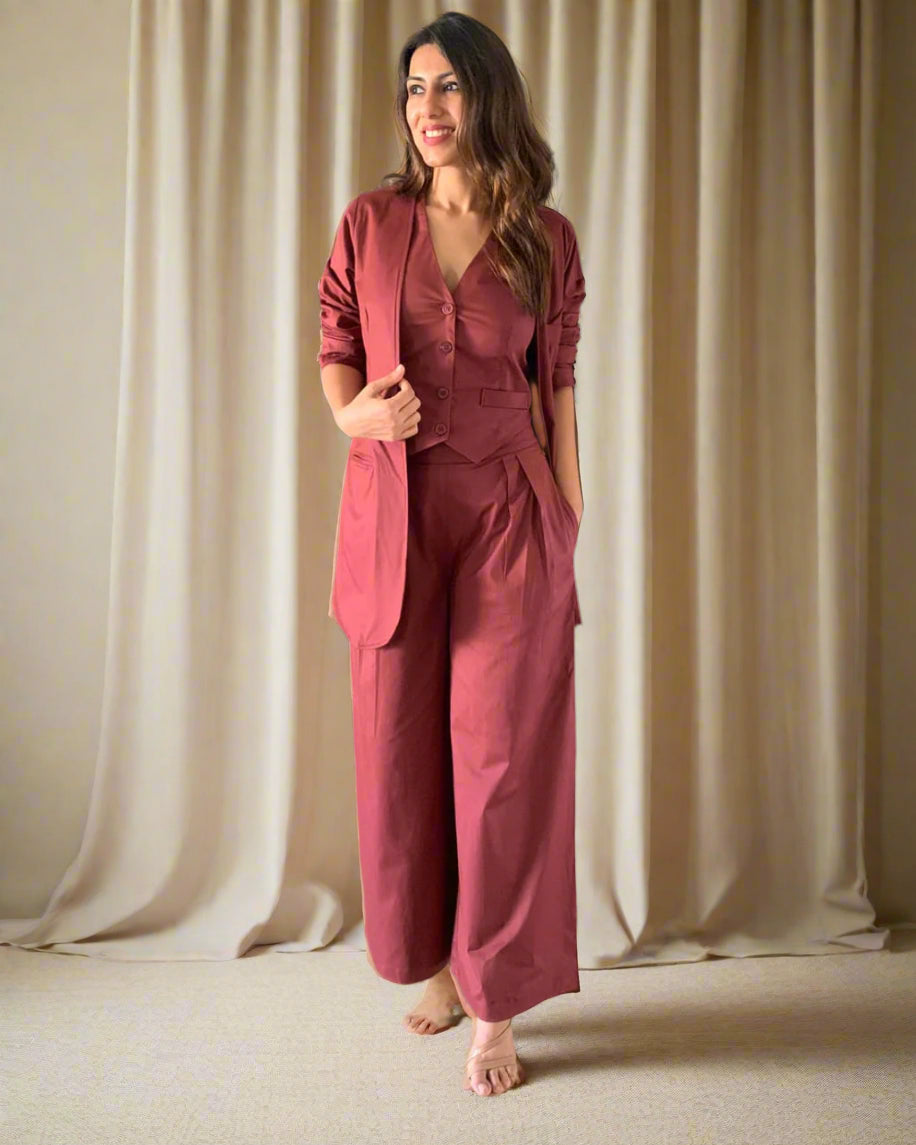 Woman in a maroon suit standing in a room with wooden flooring and decorative vases.