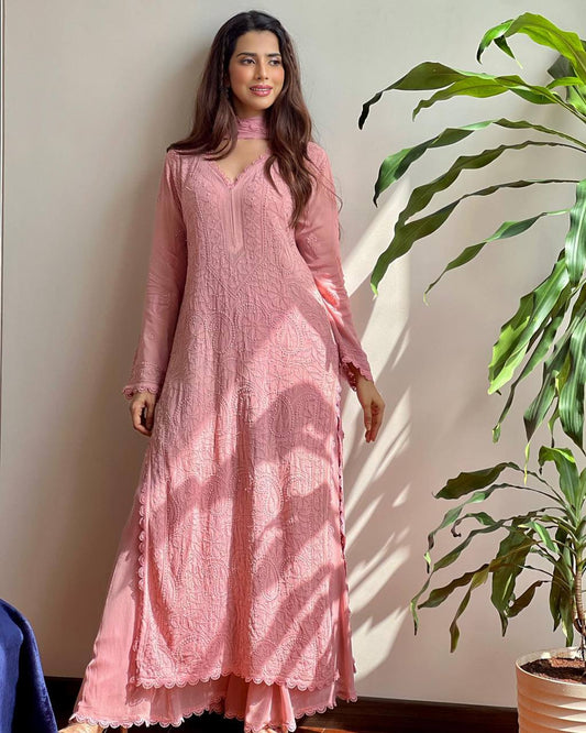 Woman in a pink traditional outfit standing next to a plant indoors.