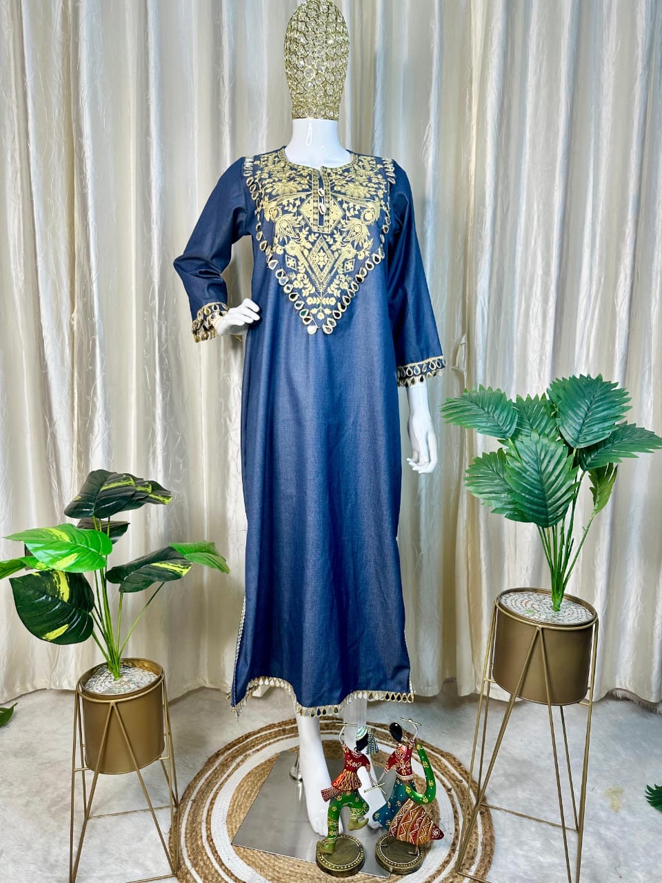 Blue dress with gold embroidery on a mannequin against a white curtain background
