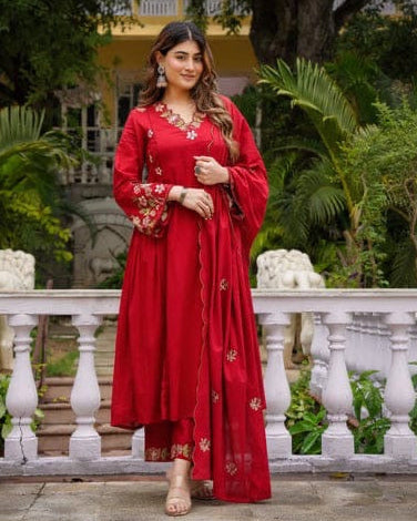 Woman in a red traditional outfit standing in a garden with greenery and a white railing.