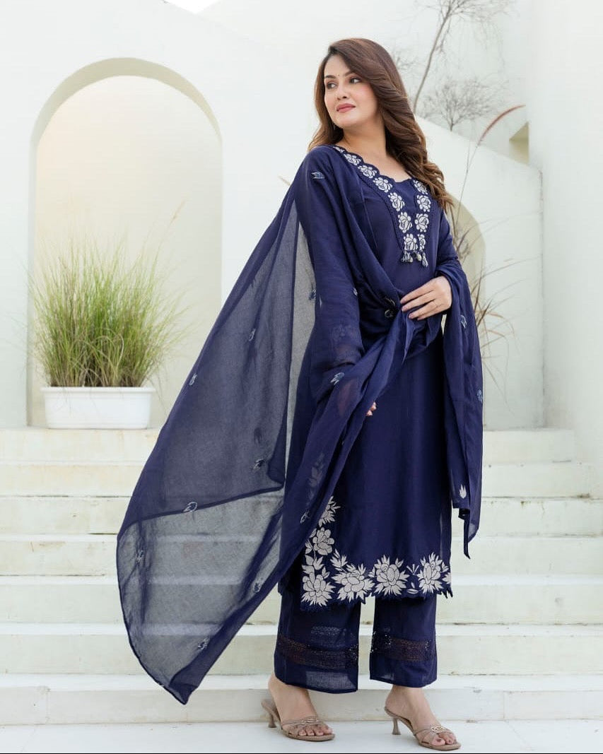 Woman wearing a navy blue embroidered outfit with a sheer dupatta on a white architectural background