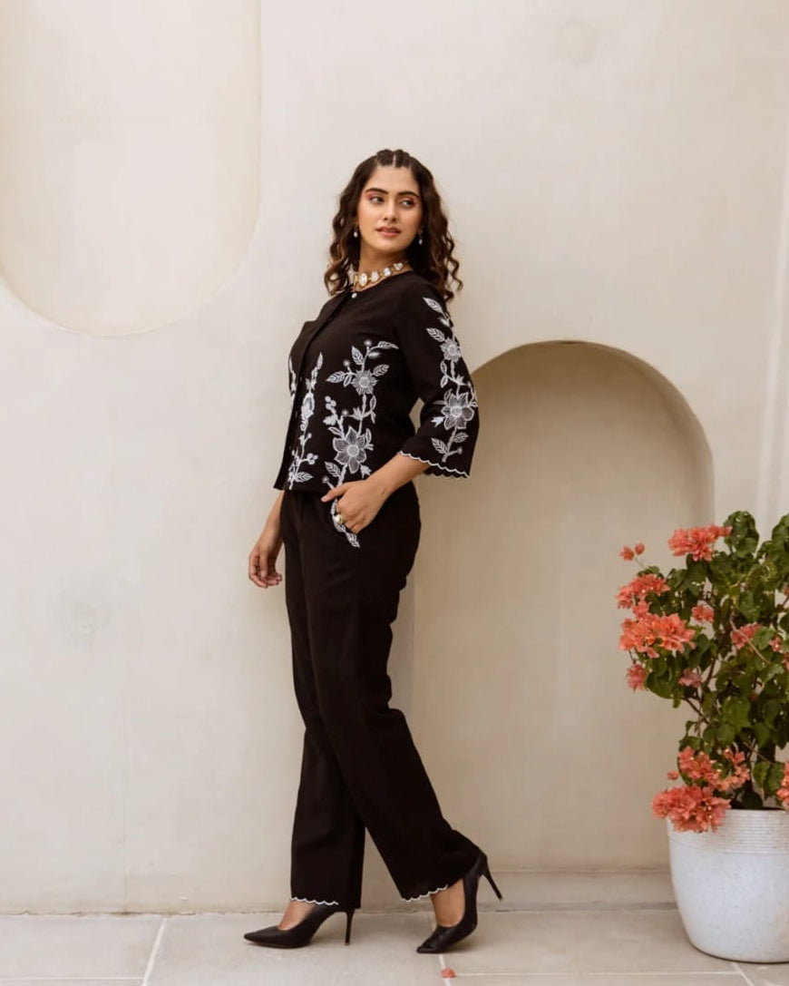 Woman in a black outfit with floral patterns standing against a white wall with a decorative arch.