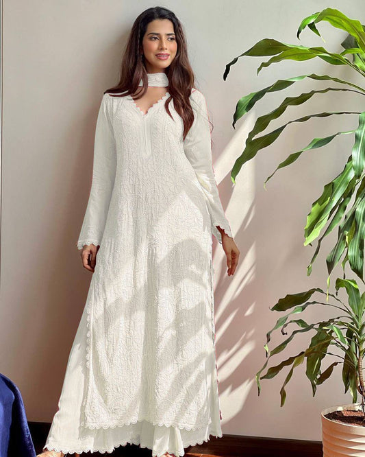 Woman in a white dress standing next to a plant indoors