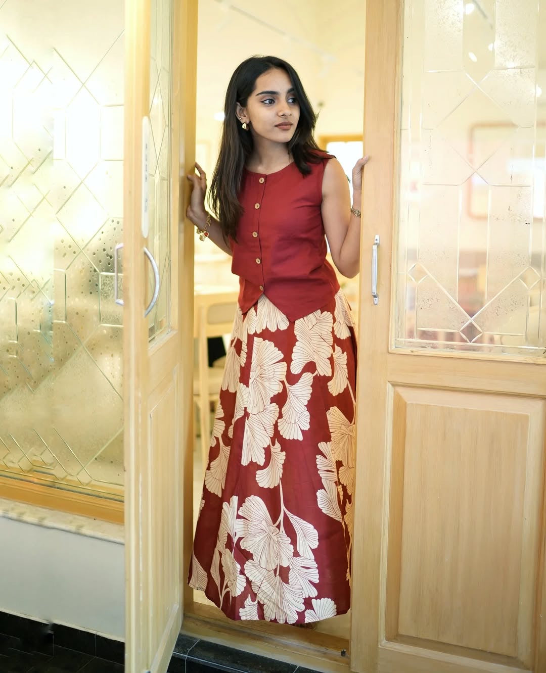 Woman in a red dress with floral pattern standing in a doorway.