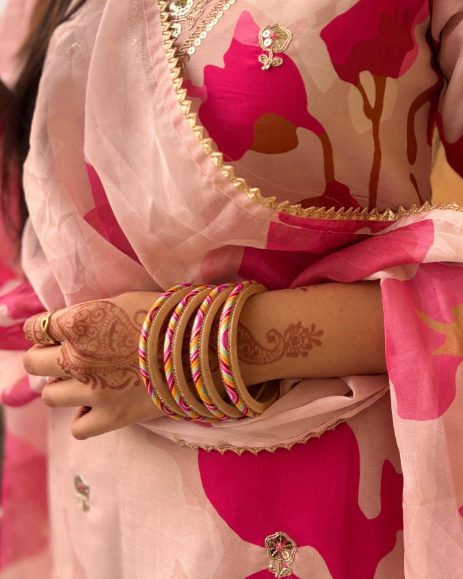 Person wearing a pink and red floral saree with gold accents, holding a phone.