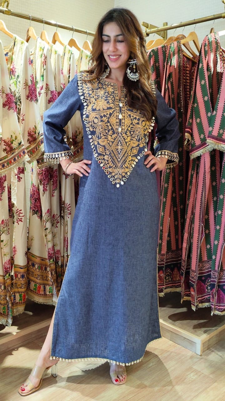 Woman wearing a blue dress with intricate gold embroidery in a clothing store.