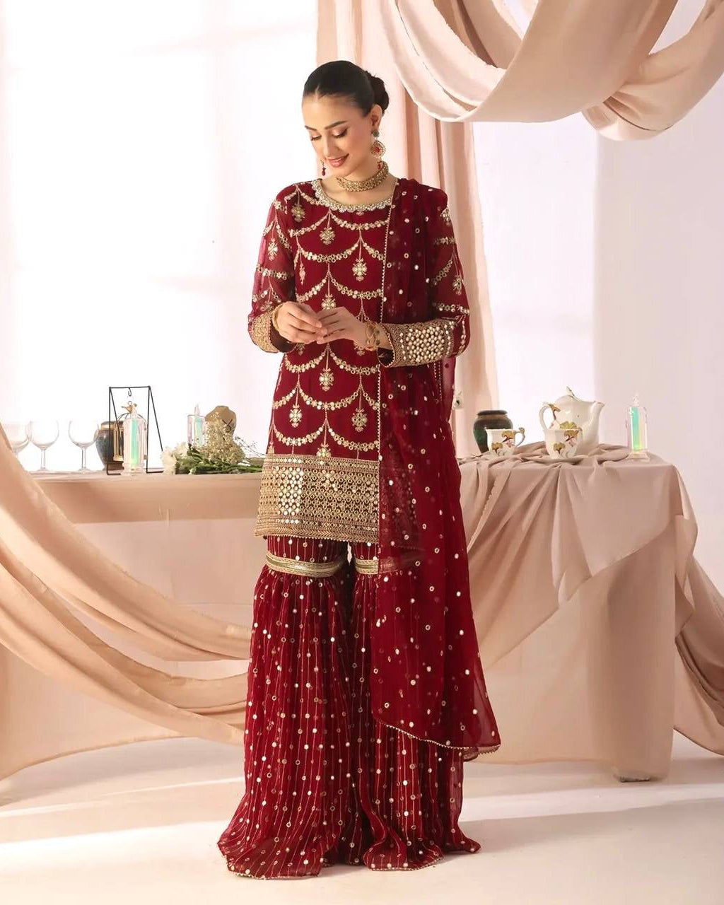 Woman in a red and gold traditional outfit standing in front of a decorated table.