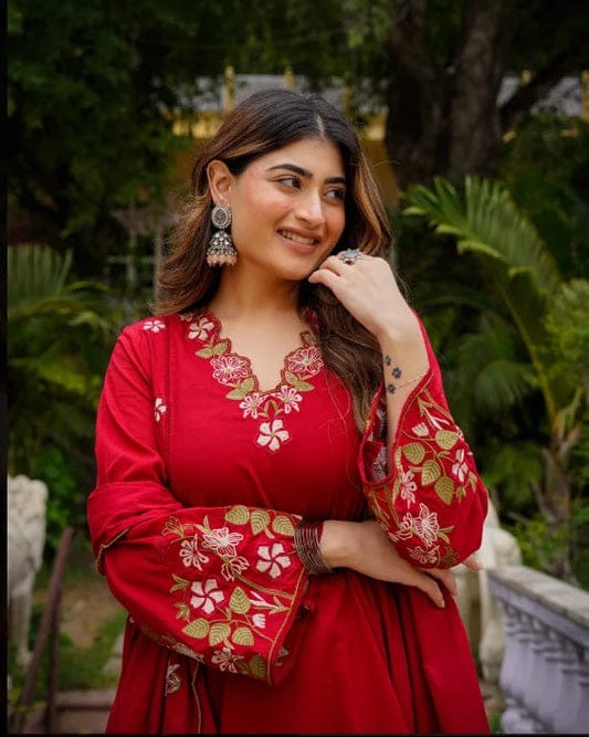 Woman in a red traditional outfit with floral embroidery standing outdoors.
