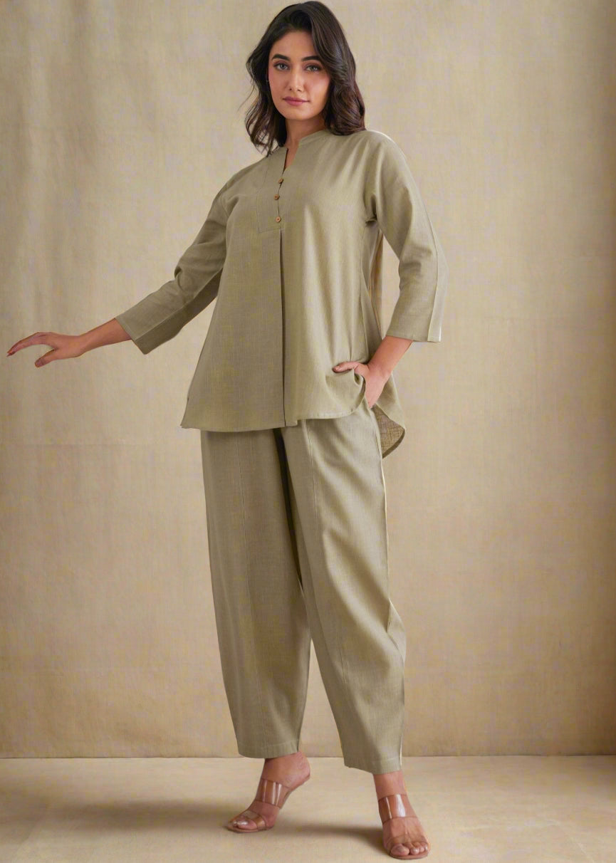 Woman wearing a green outfit standing against a decorative wall with peacock designs.