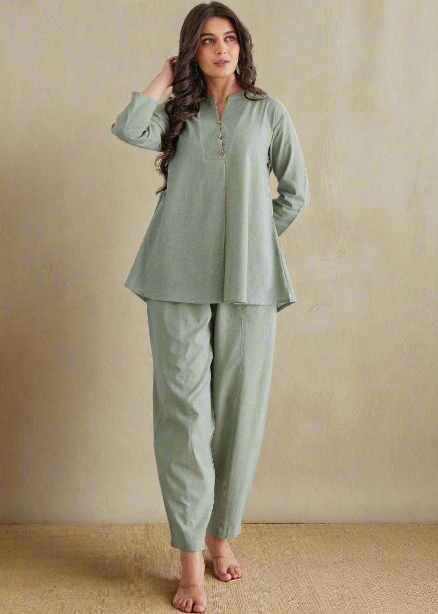 Woman wearing a green pajama set against a decorative wall.