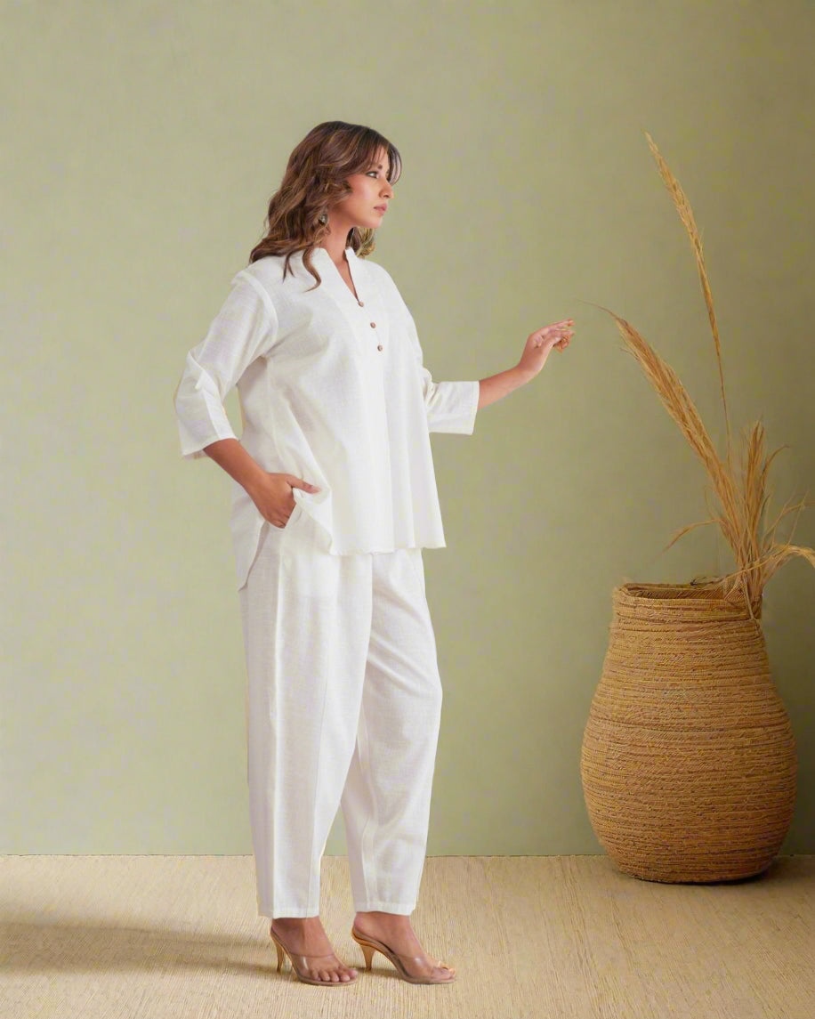 Woman in a white outfit standing against a decorative wall with leaf patterns.