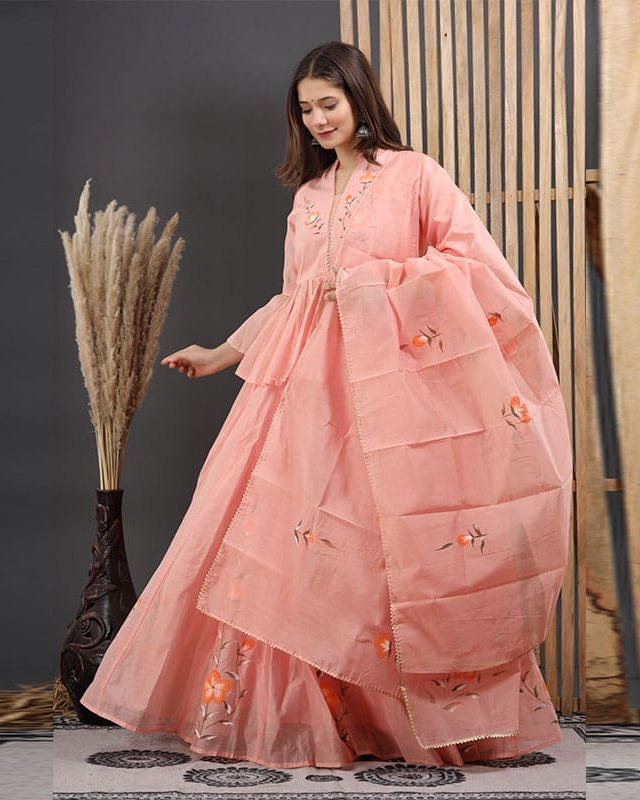 Woman in a pink traditional outfit with embroidery, standing against a dark background.