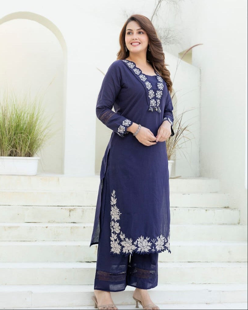 Woman wearing a navy blue embroidered outfit standing on a white staircase.