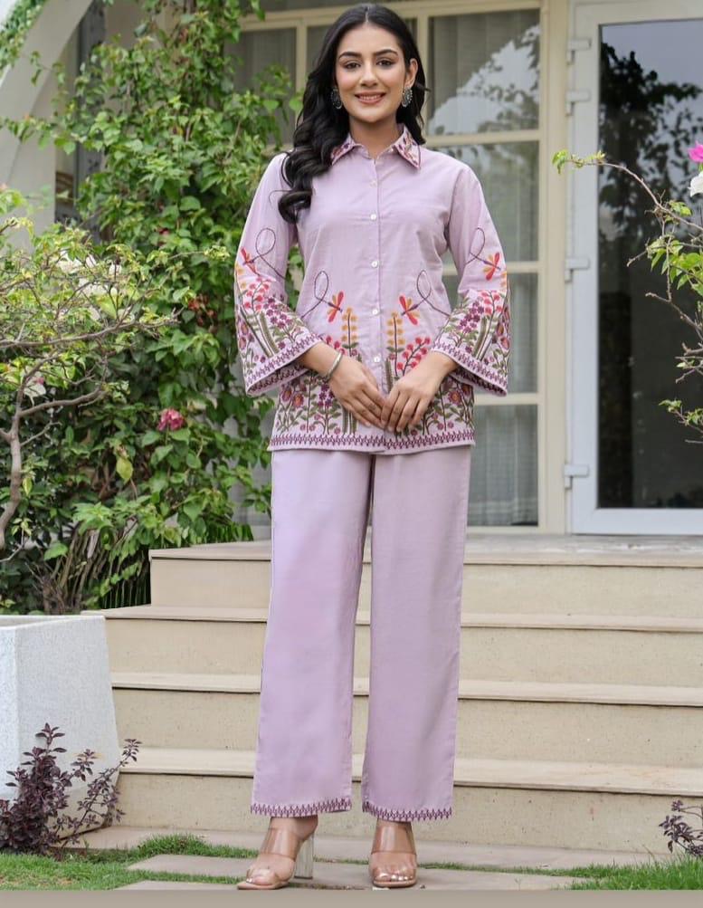 Woman wearing a pink traditional outfit with floral embroidery standing outdoors.