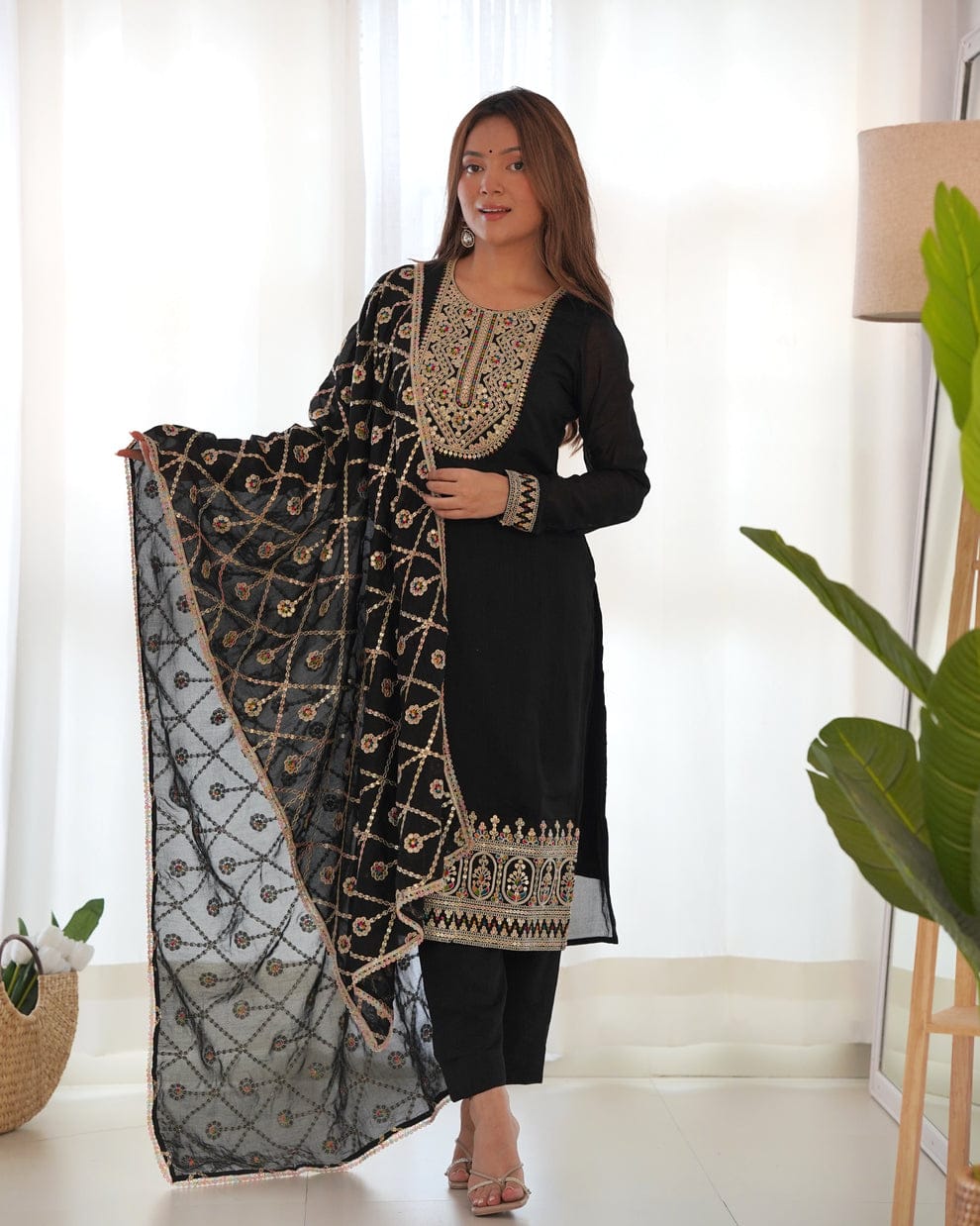 Woman holding a black and gold embroidered dupatta in a bright room.
