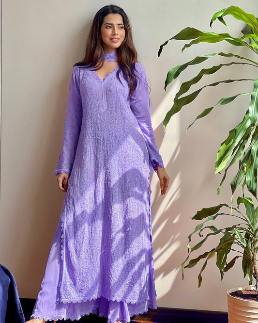 Woman wearing a purple outfit standing next to a plant indoors.